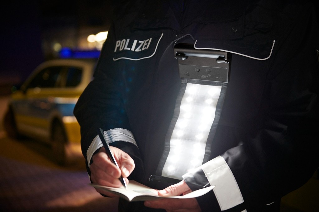 Police officer in POLIZEI jacket using chest-mounted XP FIREFLY LED light to write notes at night